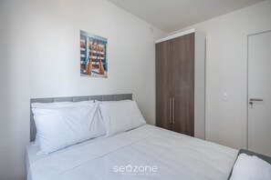 A bedroom with a bed, white bedding, a grey headboard, a wooden wardrobe, and a door. - Apart w/ BBC 750 m From the Beach Sfr0411 (Barra Velha)