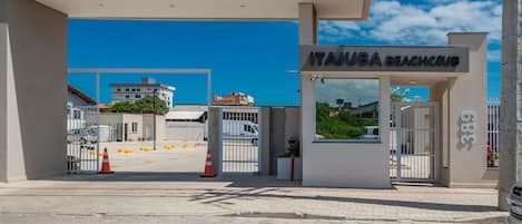 Entrada a un club de playa con un camino de acceso cerrado, cielo despejado y un edificio al fondo.