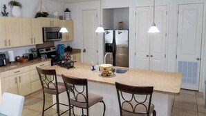 A modern kitchen with a central island, bar stools, stainless steel appliances, and pendant lighting. - Channel  views  Private Boat Slip  Pool & Patio (South Padre Island)