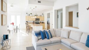A modern living room with a large L-shaped sofa, a coffee table, and a dining area with a table and chairs. - Channel  views  Private Boat Slip  Pool & Patio (South Padre Island)