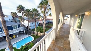 Un balcón con vista a una piscina, palmeras y casas vecinas.