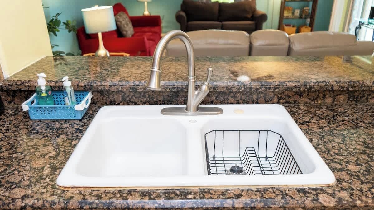 A kitchen sink with a modern faucet, a granite countertop, and a soap dispenser.