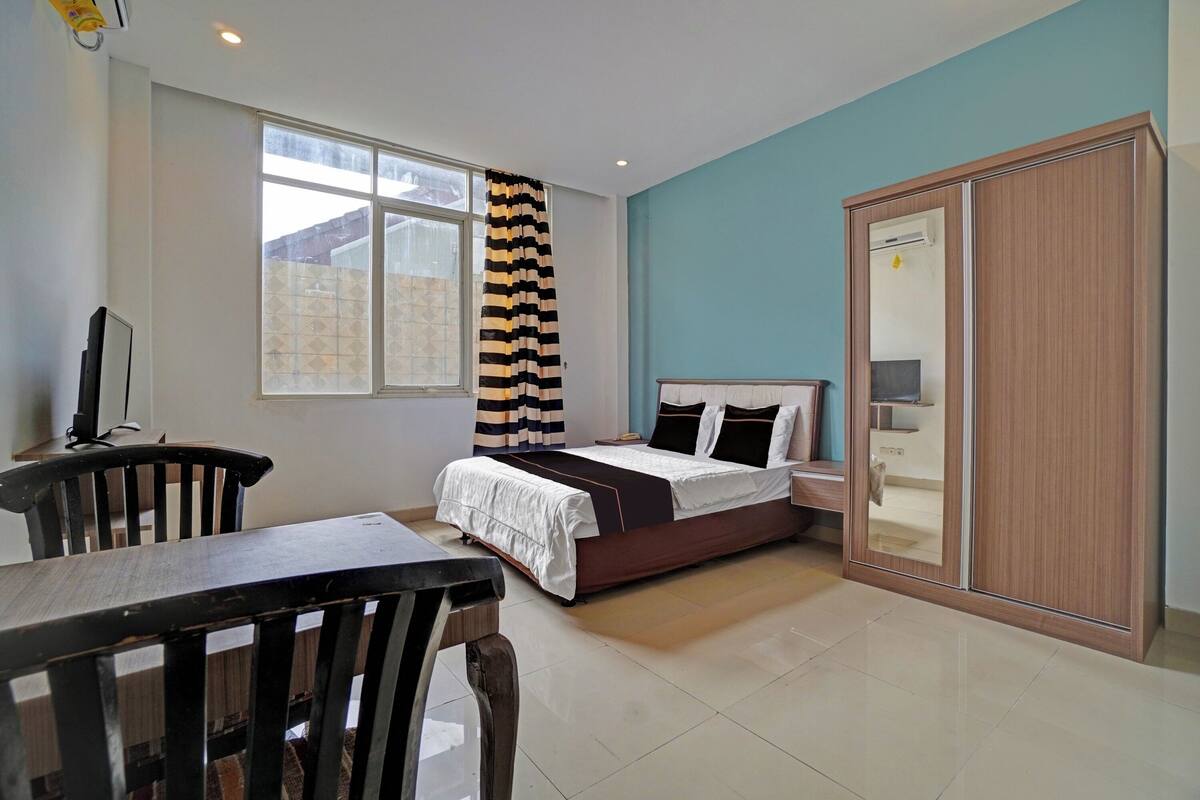 Un dormitorio con cama, escritorio, silla, armario y ventana con cortinas.