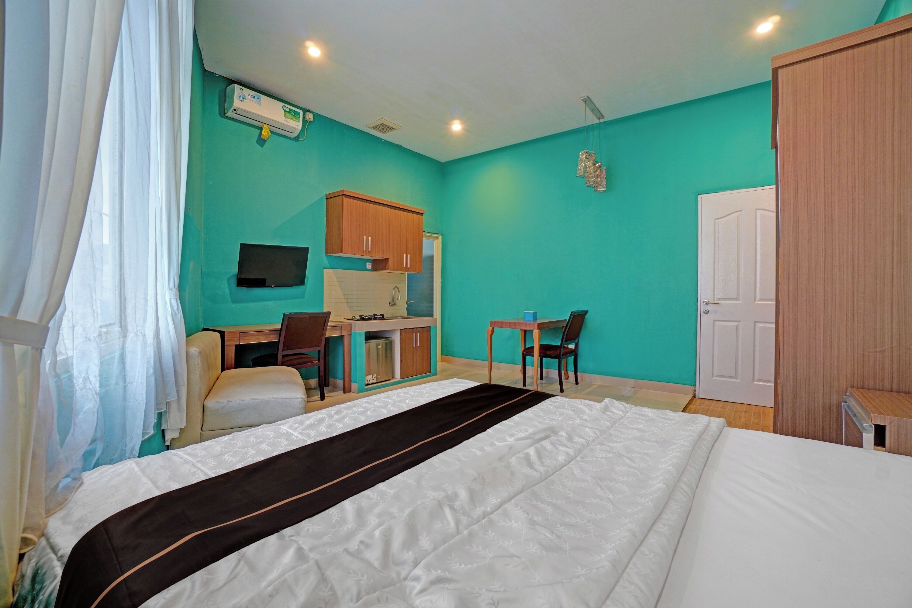 A hotel room with a bed, a desk, a chair, a small kitchenette, and a wardrobe.