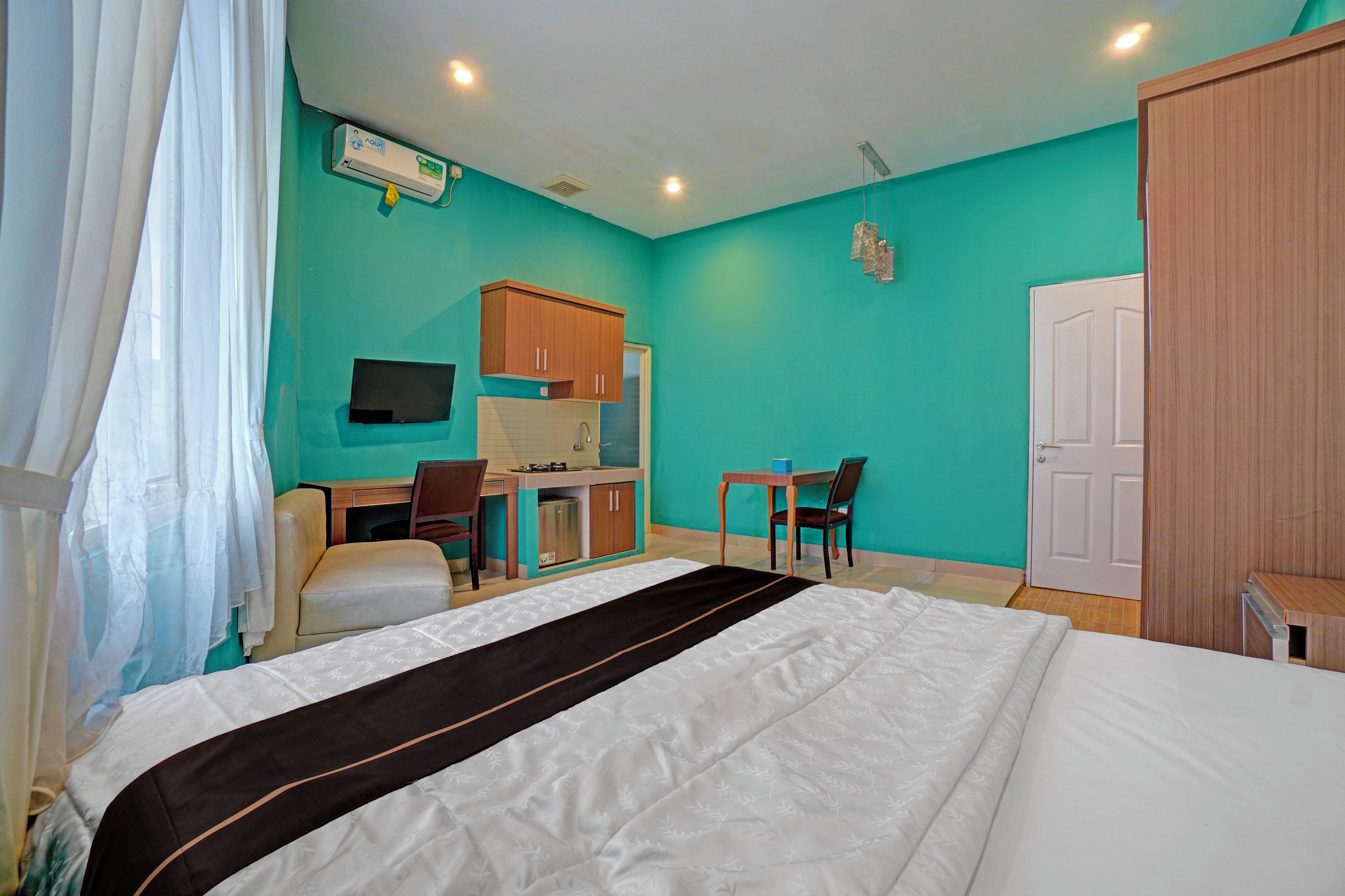 A hotel room with a bed, a desk, a chair, a small kitchenette, and a wardrobe.