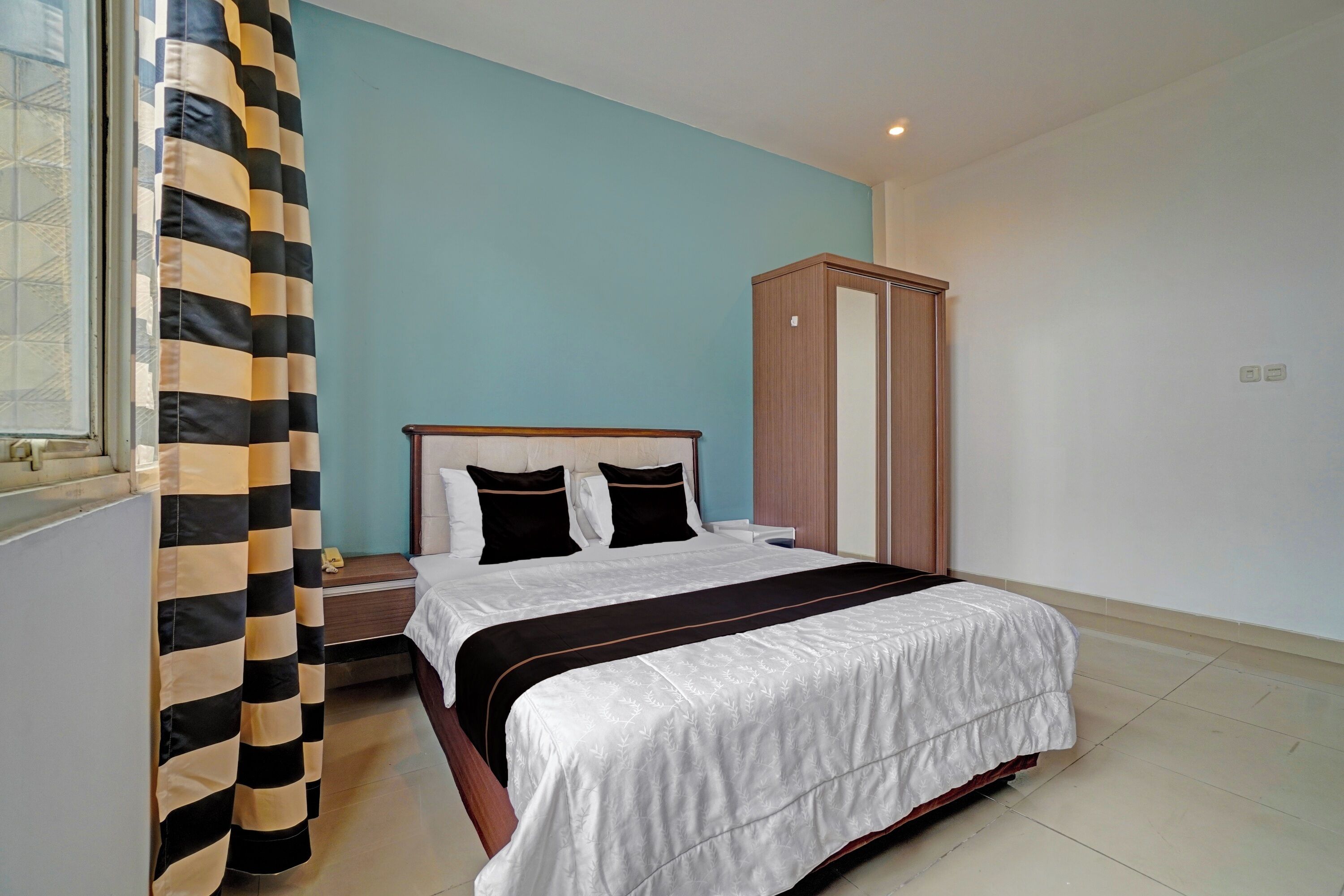 A bedroom with a bed, a wardrobe, a nightstand, and a window with curtains.