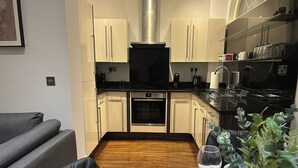 A compact kitchen with white cabinets, a built-in oven, and a black countertop. - Tavistock House-contractor Stay-parking-sleeps 7, (Bedford)