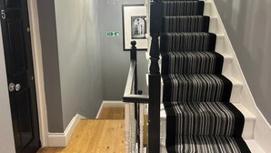 A staircase with black and white striped carpet, a chandelier, and a fire exit sign. - Tavistock House-contractor Stay-parking-sleeps 7, (Bedford)