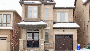 Ein zweistöckiges Haus mit Garage, Ziegelhausfassade und Schnee auf dem Dach und dem Boden.