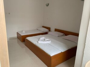 Une chambre d’hôtel avec deux lits en bois, chacun agrémenté de draps et d’oreillers blancs, et une petite table de chevet avec une lampe.