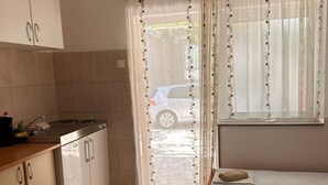 A compact kitchen with a sink, stove, and cabinets, a small dining area with a table, and a window with curtains. - Apartments Adriana Studio apartment 3 (Podaca)