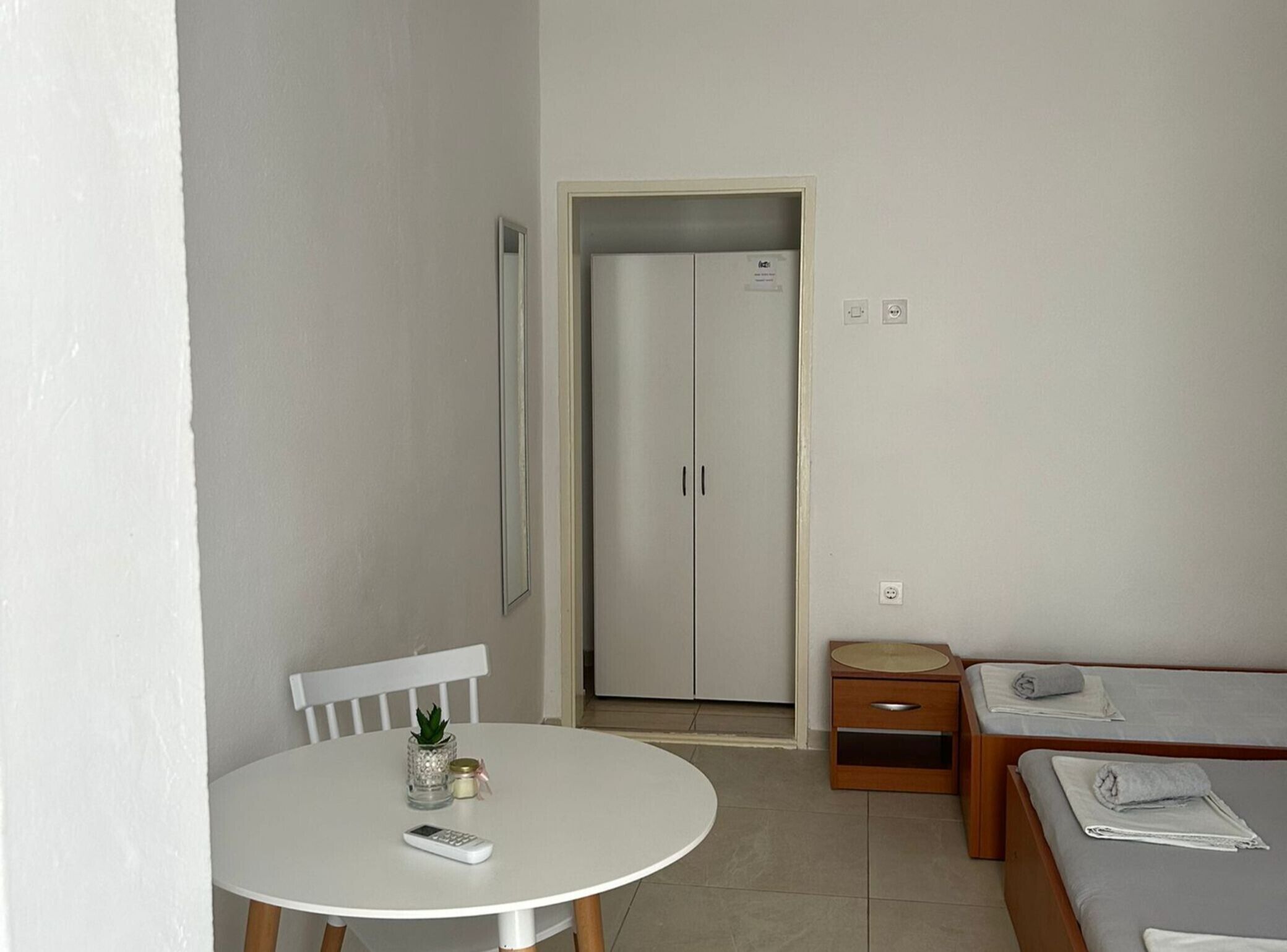 A small, clean room with a white table, a chair, a bed, and a wardrobe.
