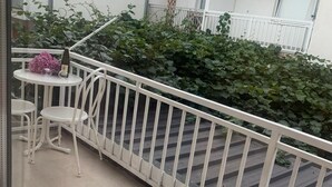 Een balkon met een witte reling, twee witte stoelen, een klein rond tafeltje en een fles champagne.