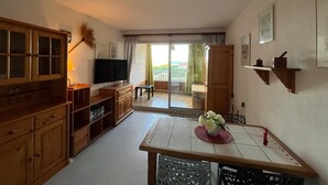 Een gezellige kamer met een houten kast, een televisie, een eettafel met een bloevas en een balkon met uitzicht.