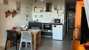 Een compacte keuken met een magnetron, oven en gootsteen. Er is een eethoek met een tafel en stoelen.