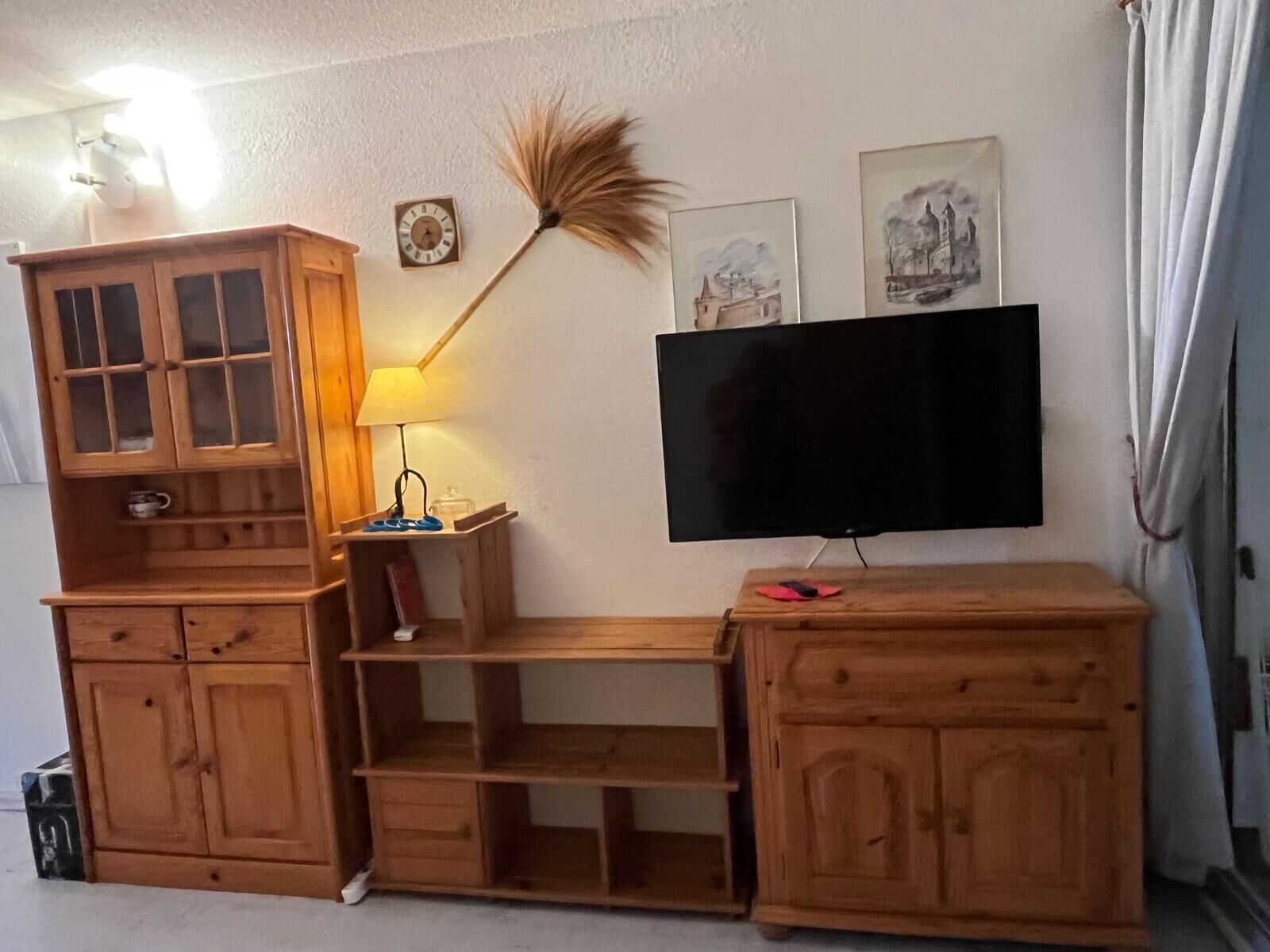 A wooden entertainment unit with a flat-screen TV, a lamp, and wall art.