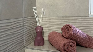 Ein Badezimmer mit Marmorwand, einer dekorativen Vase mit Rattan-Diffusor und gerollten Handtüchern.