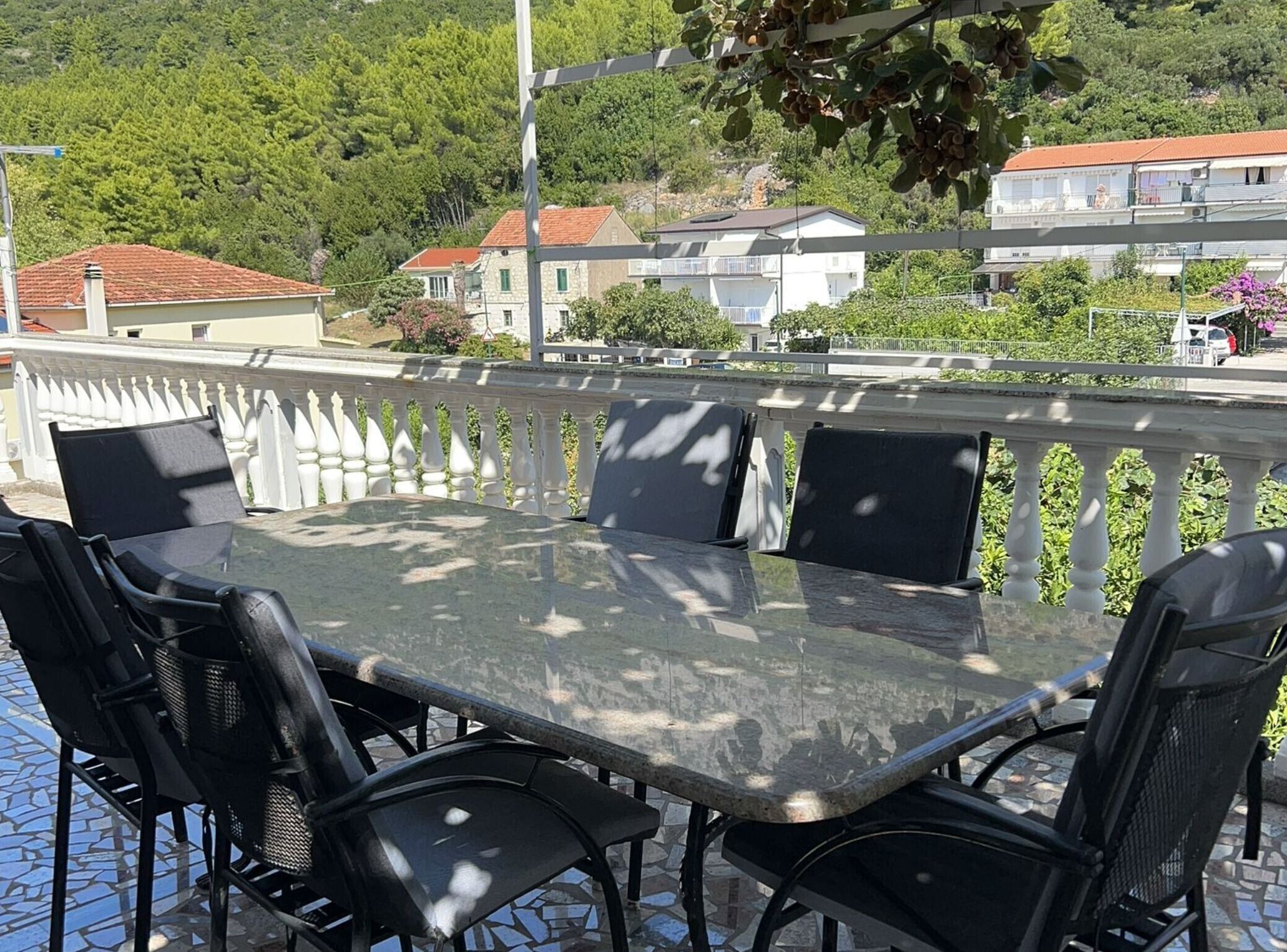 Eine Terrasse mit einem Glastisch und schwarzen Stühlen, mit Blick auf ein Wohngebiet mit Häusern und Grünflächen.