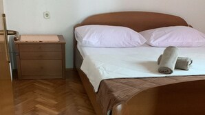 A neatly made bed with white linens and pillows, a wooden nightstand with a small drawer, and a herringbone-patterned wooden floor. - Apartments Adriana - Two bedroom Apartment Ružica 2 (Podaca)