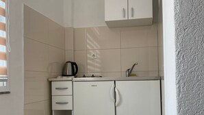 Une cuisine compacte avec des meubles blancs, un four encastré et une bouilloire.