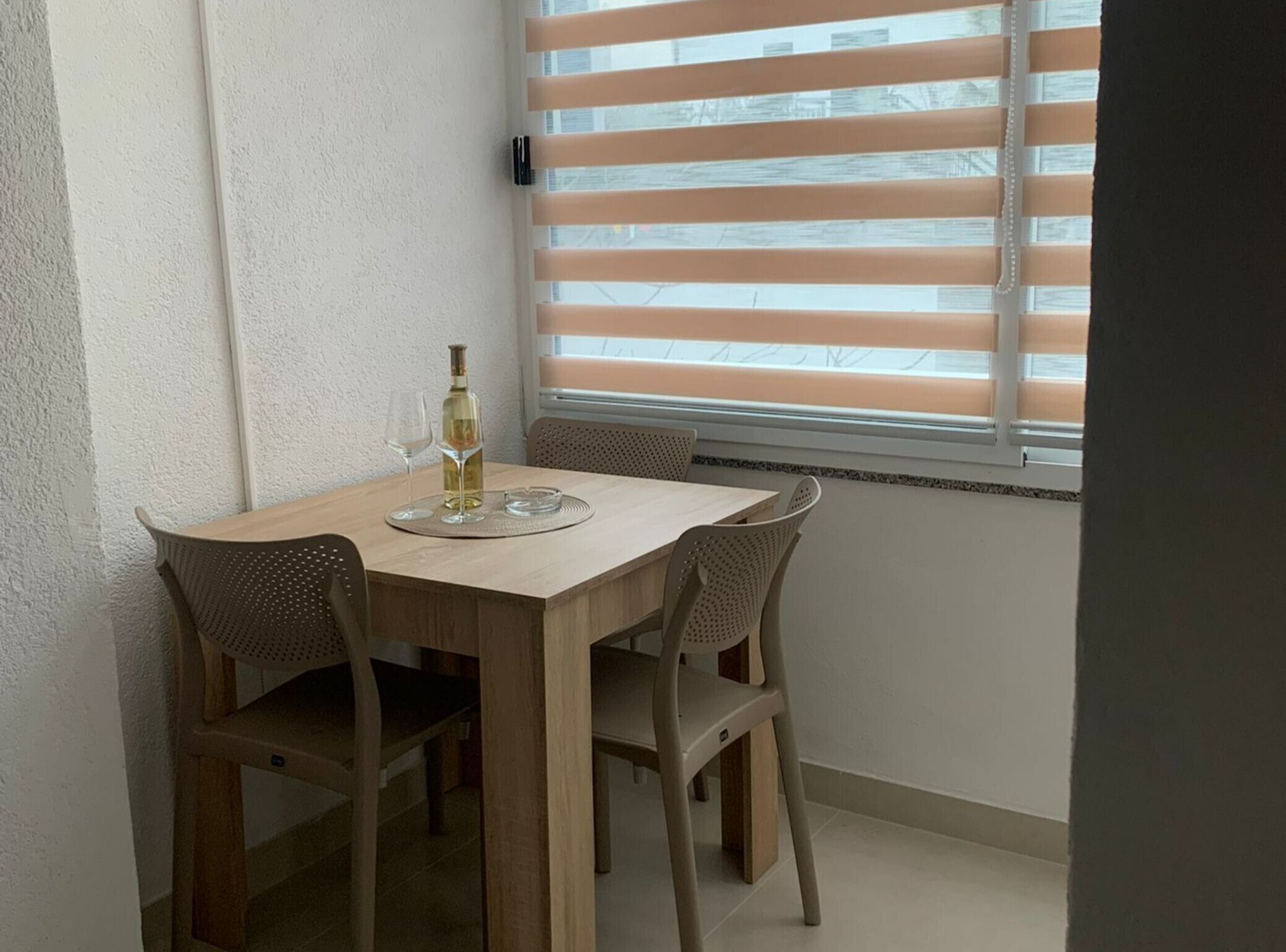 Un'area pranzo con un tavolo di legno e quattro sedie, una bottiglia di vino e due bicchieri da vino poggiati su un tappetino.