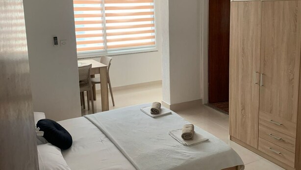 Une chambre à coucher comprenant un lit, deux serviettes, une armoire en bois, une fenêtre avec des stores et une petite table avec une chaise.