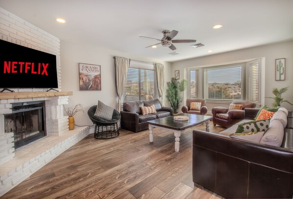 A living room with a fireplace, leather sofas, a coffee table, and a TV displaying 'NETFLIX'.