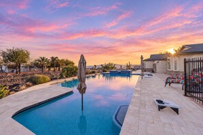 A swimming pool with a sunset view, surrounded by palm trees and a patio area with outdoor furniture.