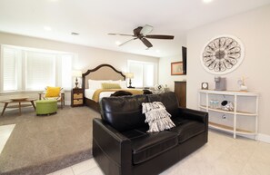 A modern living room with a black leather sofa, a ceiling fan, a coffee machine, and a decorative wall piece.