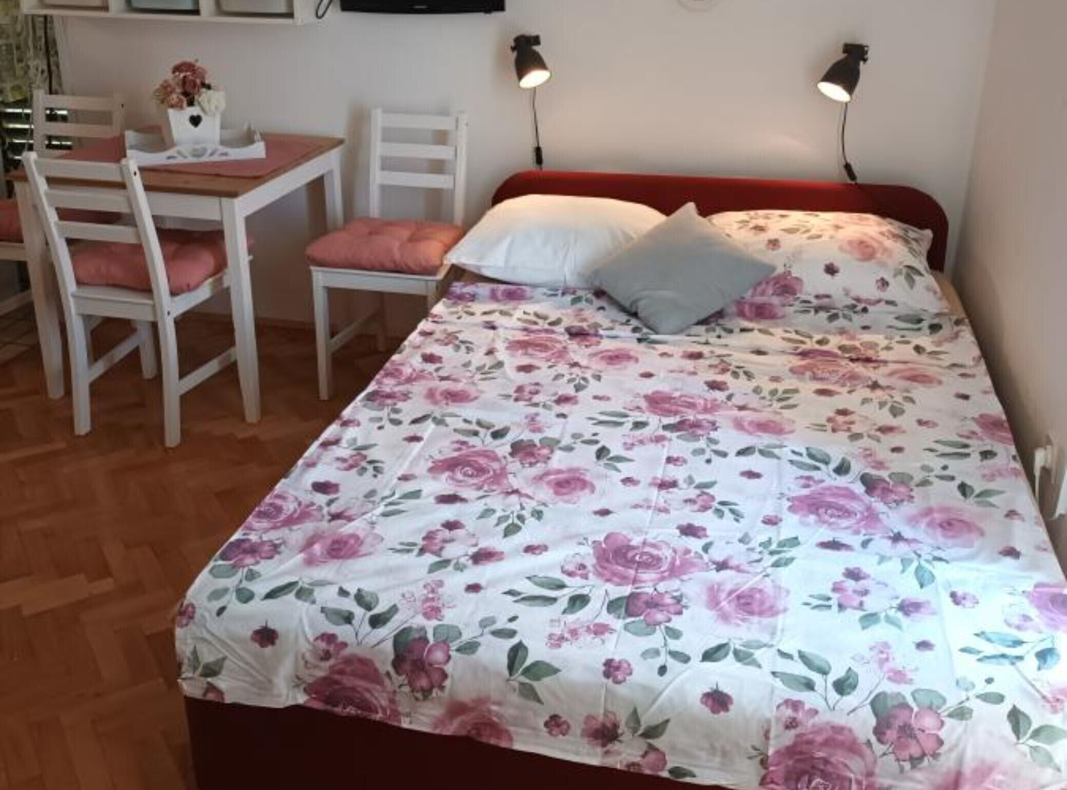 A bedroom with a floral bedspread, a wooden desk with a chair, and two bedside lamps.