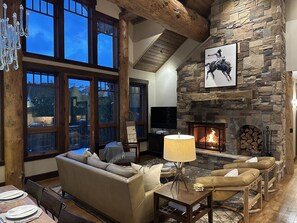 A spacious living room with a stone fireplace, large windows, and a cozy seating area. - Fabulous New Rental 5-bedroom 5.5 bath house, with private ski in/out lodge (Big Sky)