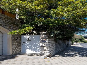 Ein Gebäude aus Stein mit einer weißen Tür, einer Steinsäule und einem Baum, der Schatten spendet.