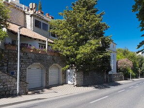 Straßenansicht eines steinernen Gebäudes mit einem Ziegeldach, einem großen Baum und blauem Himmel.