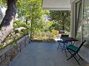 Eine Terrasse mit Tisch und Stühlen, eine Steinmauer und Blick auf eine Hügellandschaft.