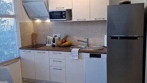 Una cocina moderna con armarios blancos, un refrigerador de acero inoxidable, un microondas y un frutero en la encimera.