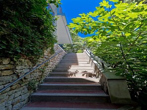 Eine Treppe mit Steinsäulen an einer Seite und einem Metallgeländer, die zu einem Gebäude mit einer blauen Tür führt.