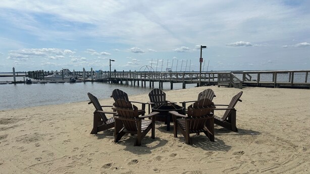 Une plage avec des chaises Adirondack en bois disposées autour d’une table, une jetée qui s’avance dans l’eau et un ciel dégagé.