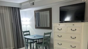 Une pièce comprenant une table à manger, des chaises, un téléviseur posé sur une commode et une lampe.