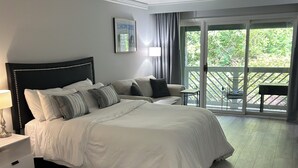 Une chambre avec un grand lit, une table de chevet, une lampe, une chaise et une vue sur l’extérieur grâce à une porte-fenêtre coulissante.