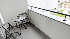 Un balcón con una mesita, dos sillas, una planta en maceta y vistas a un edificio y follaje.
