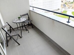 Ein Balkon mit einem kleinen Tisch, zwei Stühlen, einem Blumentopf und Blick auf ein Gebäude und Grünflächen.