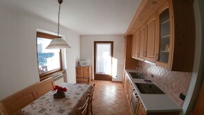 A compact kitchen with wooden cabinets, a dining table with a checkered tablecloth, and a window with a view. - Baita la Malgheta - Bormio, mountains, skiing and relaxation (Piatta)