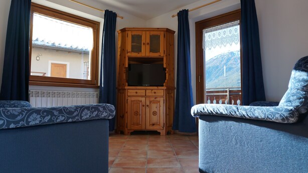 A corner room with a wooden cabinet, two blue upholstered chairs, and a window with curtains. - Baita la Malgheta - Bormio, mountains, skiing and relaxation (Piatta)