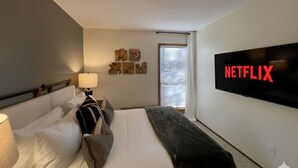 A hotel room with a bed, a TV mounted on the wall, and a window with blinds. - Sunriver Home · Hot Tub · AC · Bikes · SHARC Passes · EV Charger · BBQ (Sunriver)