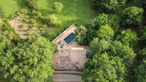 Vista aérea de una propiedad con piscina, patio cercado y abundante vegetación alrededor.