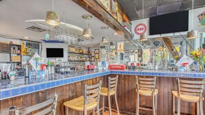 Eine Bar mit einem blau gefliesten Tresen, Holzstühlen und einer Auswahl an Flaschen und Gläsern.