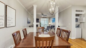 Un comedor con mesa y sillas de madera, una araña y citas enmarcadas en la pared.