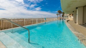 A clear blue pool with a metal railing, palm trees, and a building in the background. - Island Tower 903	|  Beach View (Gulf Shores)