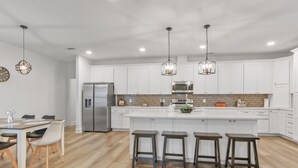 Una cocina moderna con armarios blancos, un refrigerador de acero inoxidable, una isla central con taburetes e iluminación colgante.