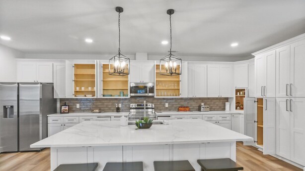 Cocina moderna con armarios blancos, una isla grande con taburetes de bar, electrodomésticos de acero inoxidable e iluminación colgante.